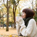Autumn woman drinking coffee under fall foliage = Shutterstock