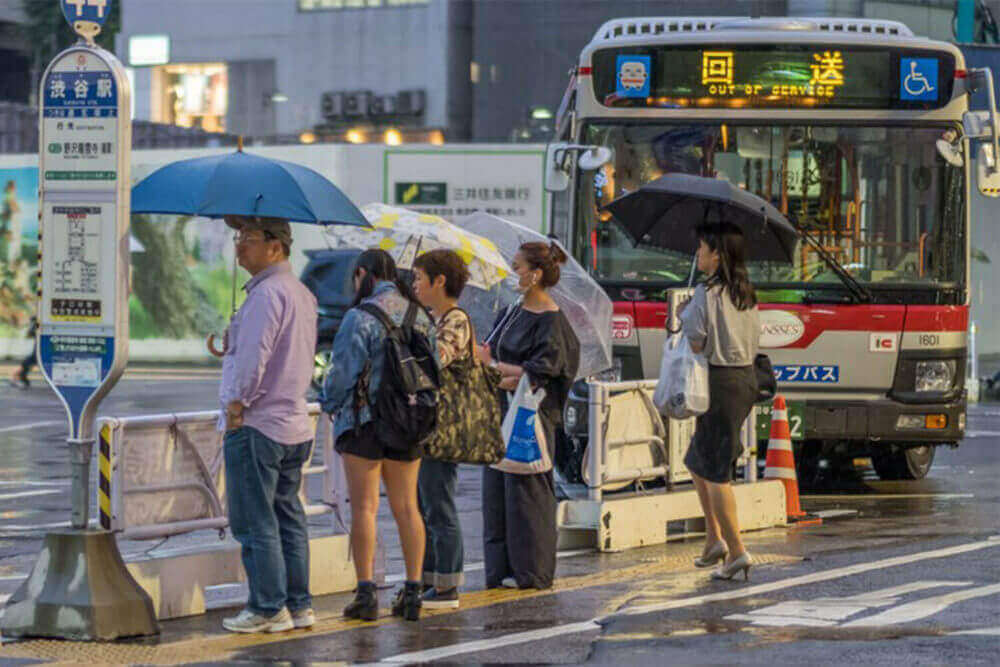 People lining up for the bus during a rainy night at Shibuya station. The rainy season, locally known as tsuyu or baiyu, begins the from June until mid July in Japan = Shutterstock
