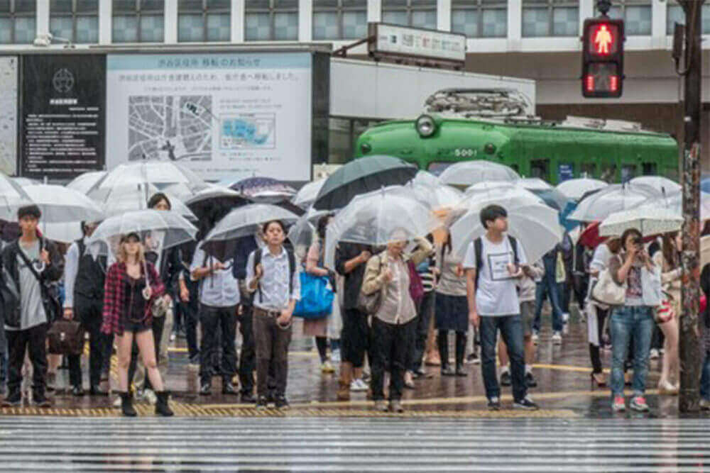 People waiting to cross Shibuya Crossing in Tokyo in a rainy day = Shutterstock