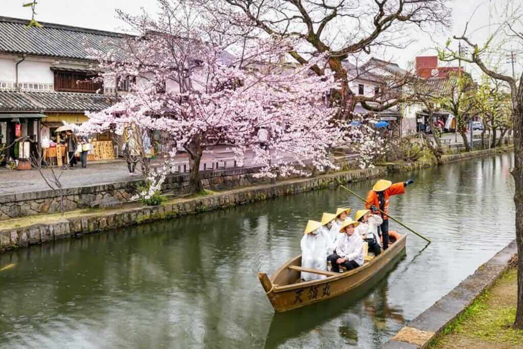Unknown tourists are enjoying the old-fashioned boat along the Kurashiki canal in Bikan district of Kurashiki city, Japan = Shutterstock