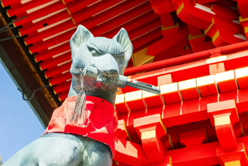 Fushimi inari stone fox guarda wooden gates. Foxes are believed to be messengers of god = shutterstock