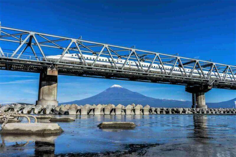The Tokaido Shinkansen bullet train passing through Mount Fuji and the Fujikawa bridge with blue sky background = shutterstock