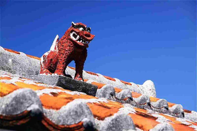 Okinawa Ryukyu style roof with a sculpture of Shasa mythical lion dog with blue cloudy sky in Okinawa island, Japan = shutterstock