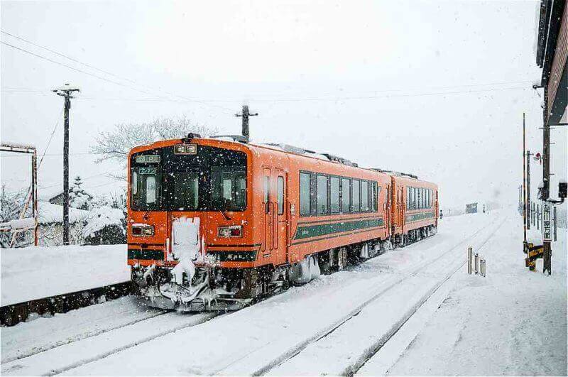 Orange color Train on snow covered tracks of Tsugaru railway line in mid winter at Goshogawara station, Aomori, Tohoku, Japan = shutterstock