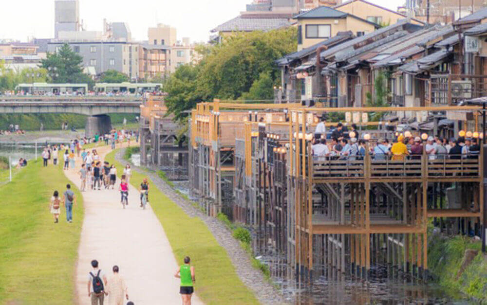 People walking around the river ” Kamogawa”. The building on the right is called "Yuka", the local restaurant seats in a location where the river can be seen outdoors, Kyoto, Japan = shutterstock