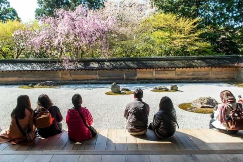 Japanese tourists enjoy tranquility at Ryoanji Temple in Kyoto, Japan. This Zen Buddhist temple is famous for its rock garden = shutterstock_1131112448