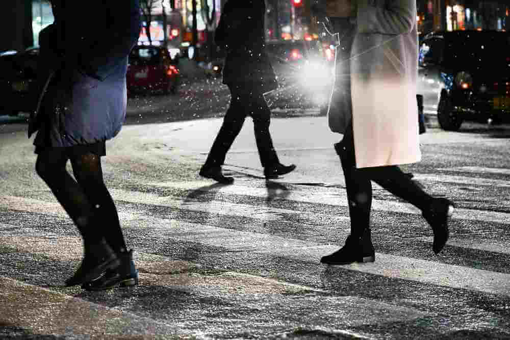 A pedestrian crossing the frozen road surface at night. January 2017 Sapporo city center Hokkaido, Japan = Shutterstock