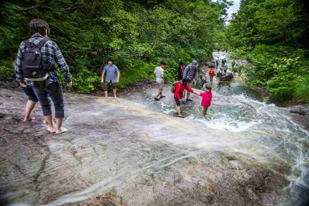 August10, 2017: The natural hotspring-fed warm waters of Kamuiwakka Falls draw visitors to walk through its waters, Shiretoko, Hokkaido, Japan = Shutterstock