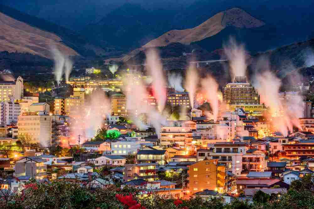 A night view of the hot spring area seen from the Yukemuri Observatory in the Kannawa district of Beppu city. Steam is illuminated in various colors, and a fantastic world spreads = Shutterstock