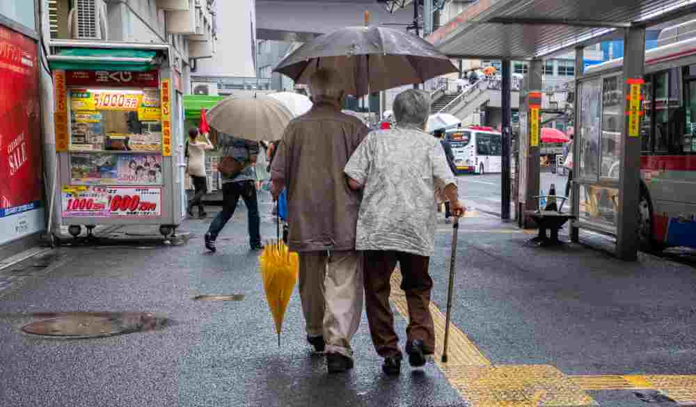 JULY 4TH, 2018. Old Japanese couple walking at a bus stop with umbrella during a rainy day, Shibuya, Tokyo = Shutterstock