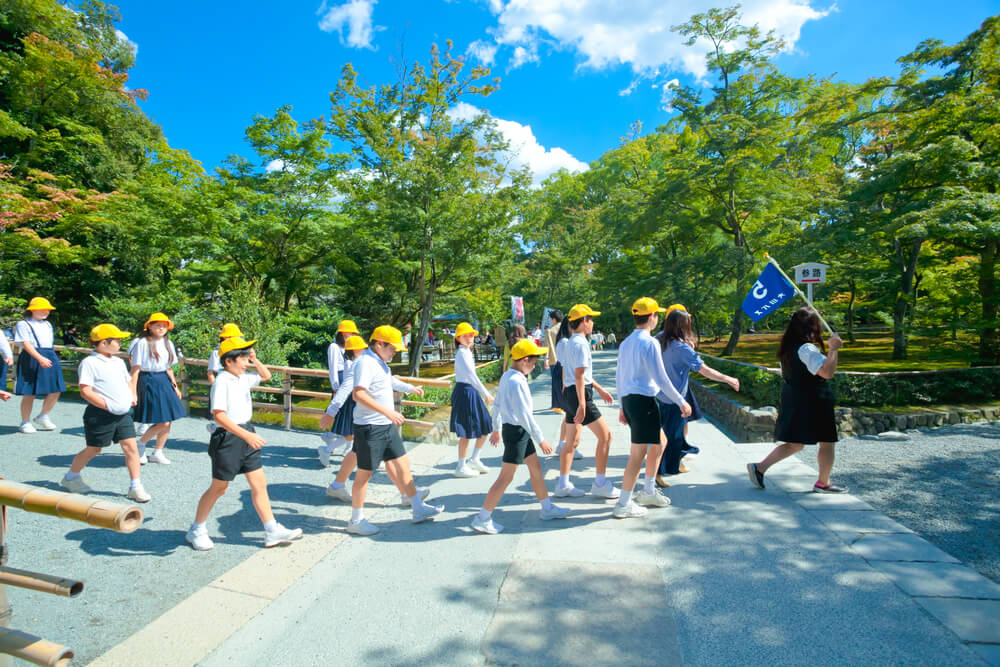 October 1 2017: A group of school kids with their teacher on a field trip to Osaka Castle. Every students must wear a yellow hat when stay outside the school, Osaka,Japan = Shutterstock