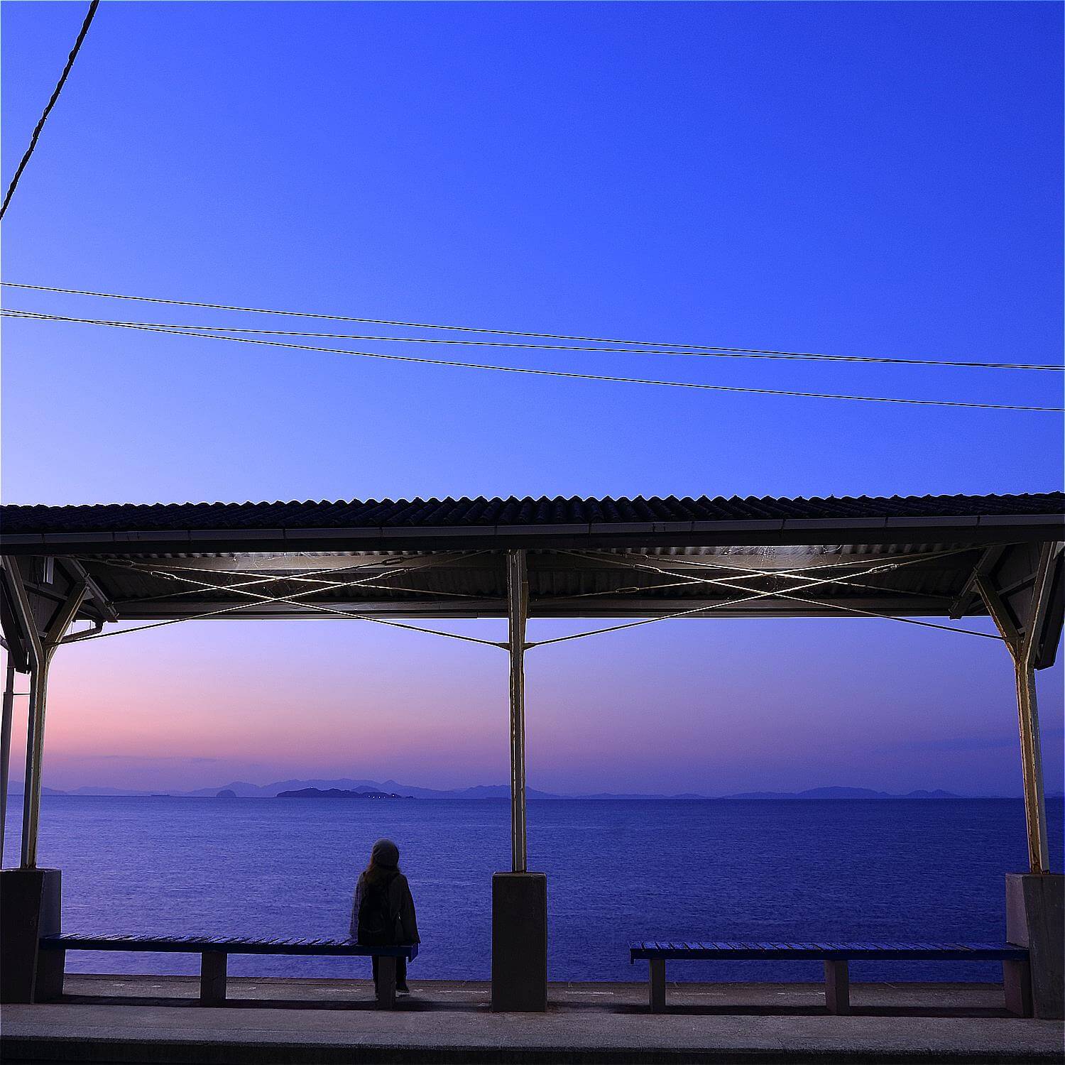 A woman traveler sit along in a beautiful seaside train stations by the sea in Shimonada, Iyo, Matsuyama, Shikoku = Shutterstock