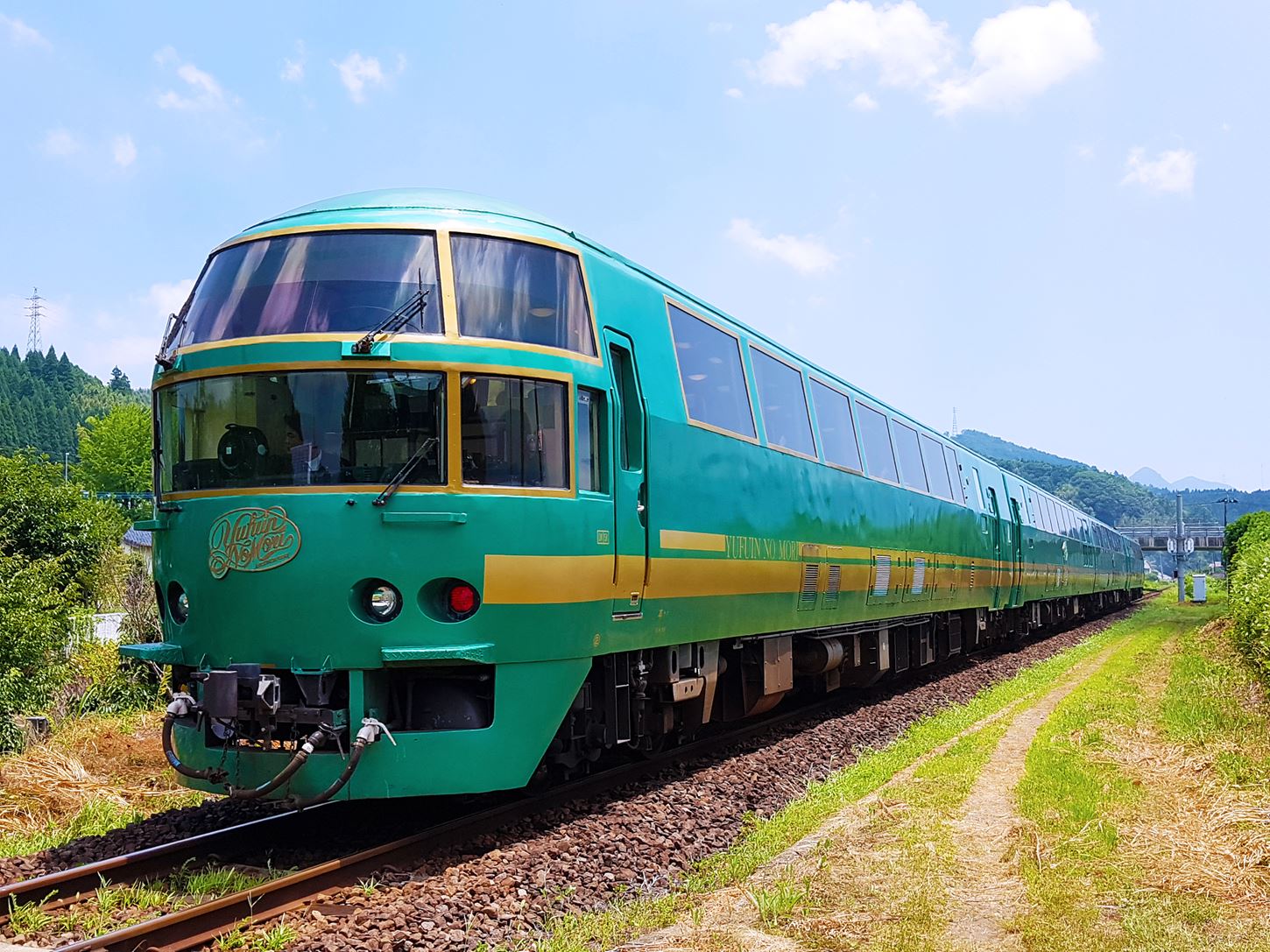 The vintage green romance train named "Yufuin no Mori" running pass the green meadow to Yufuin Station = Shutterstock